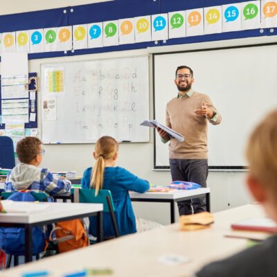 Smiling,Teacher,Holding,Textbook,Pointing,Towards,Boy,Raising,Hand,To Smiling,Teacher,Holding,Textbook,Pointing,Towards,Boy,Raising,Hand,To